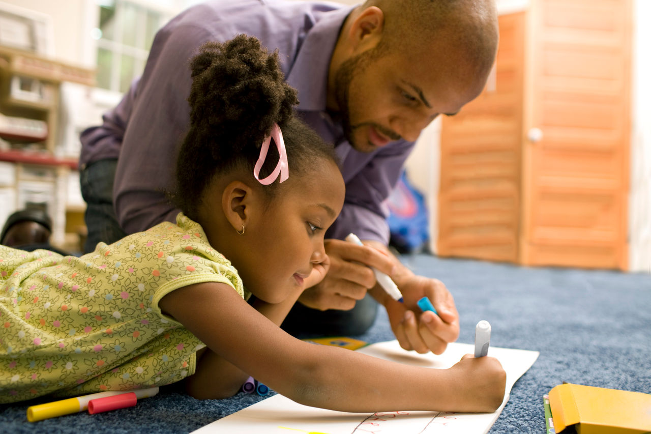 Father and daughter color a picture on the floor of their home