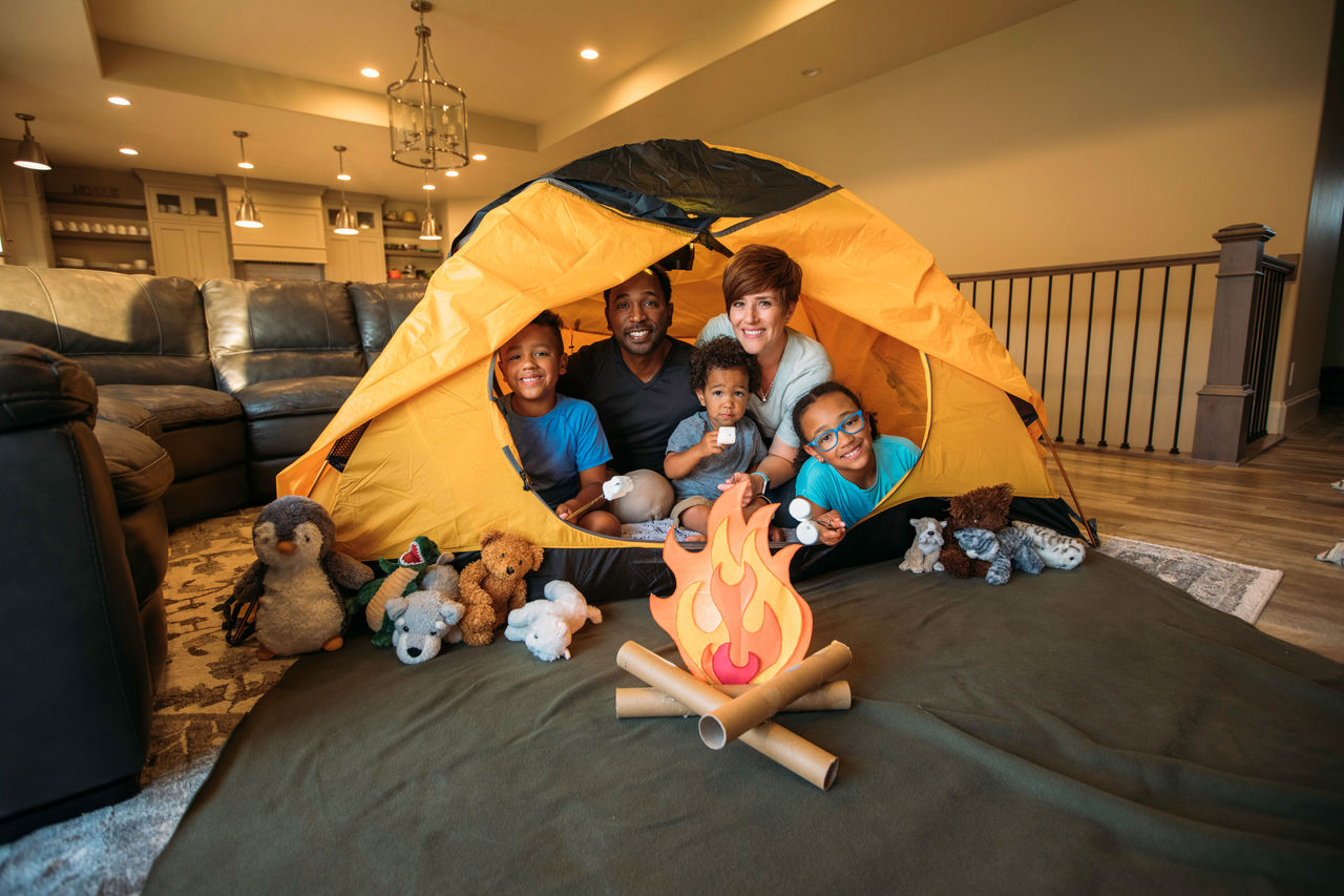 A family "roasting" marshmallows on a fake campfire from a tent in their living room