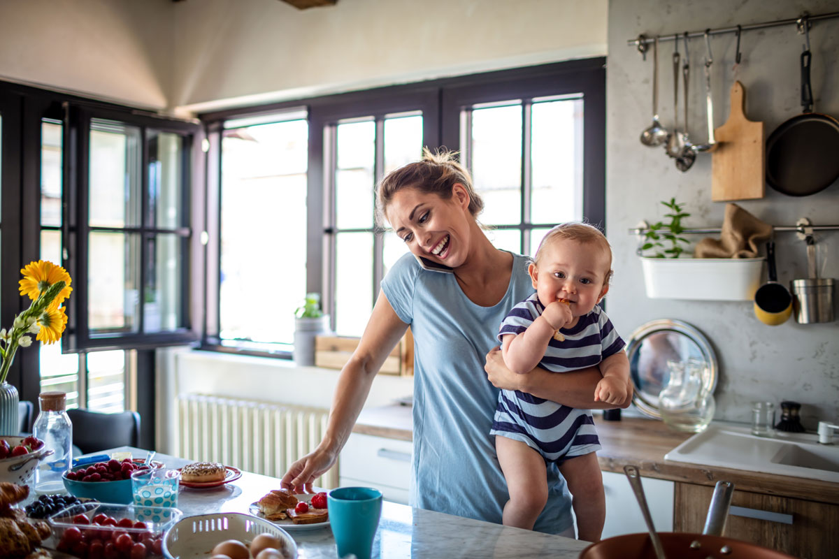 A busy mother on the phone while holding her baby and preparing breakfast